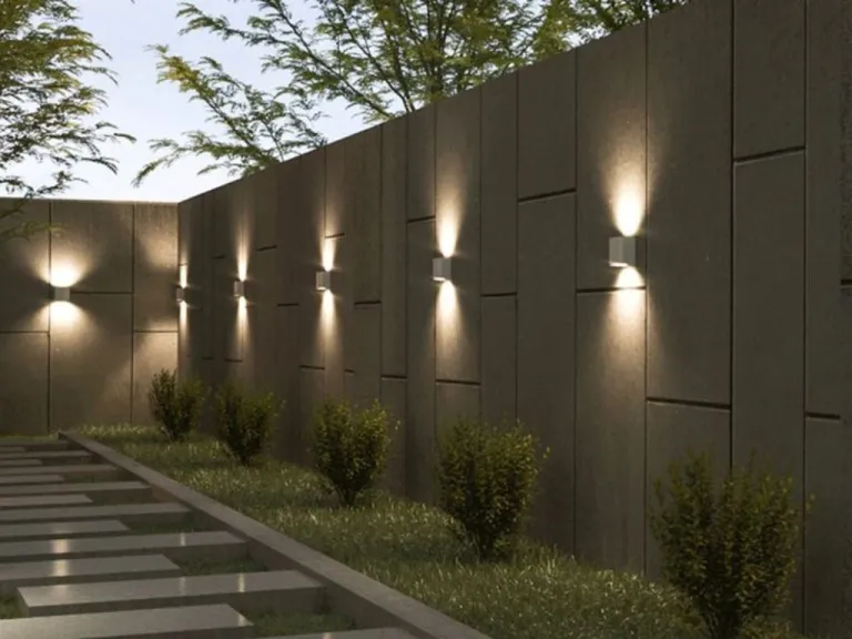 Row of up-and-down cube wall luminaires grazing a concrete boundary wall at dusk