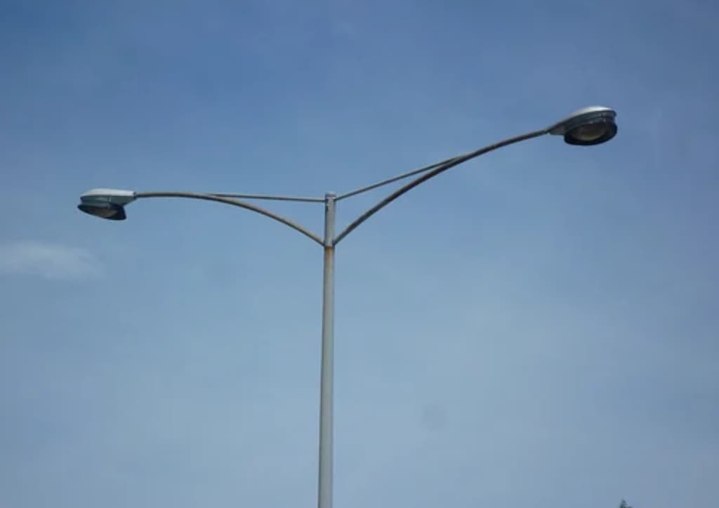 Twin-arm roadway luminaire on a tapered steel column against a clear sky
