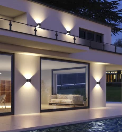 Modern rendered house exterior at dusk with a row of up/down wall luminaires grazing warm hourglass patterns onto white walls, large glazing and a pool in the foreground