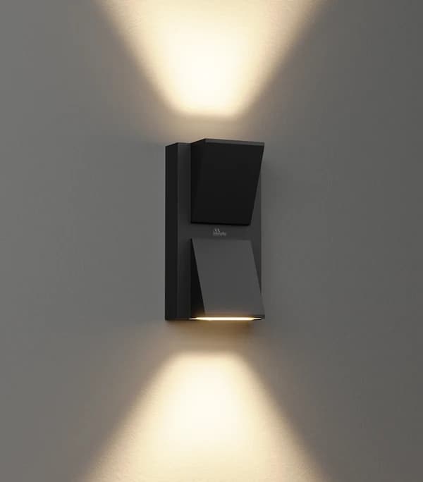Black faceted up/down wall luminaire on a grey wall throwing warm triangular beams up and down